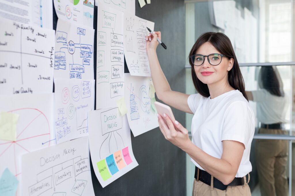Pretty young smiling business coach with smartphone preparing for seminar